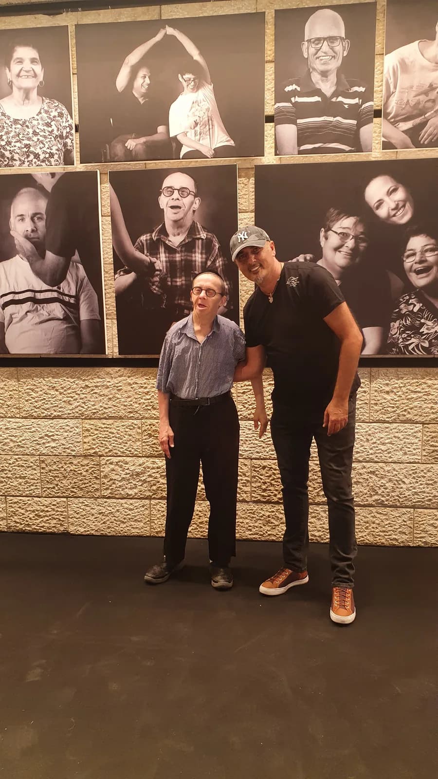 מבקרים מצטלמים מול הפורטרטים בשחור-לבן התלויים על קיר האבן בתיאטרון ירושלים