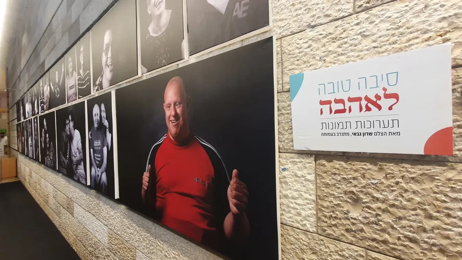 מסדרון הפורטרטים לאורך קיר אבן ירושלמית בתיאטרון ירושלים, לצד שלט התערוכה