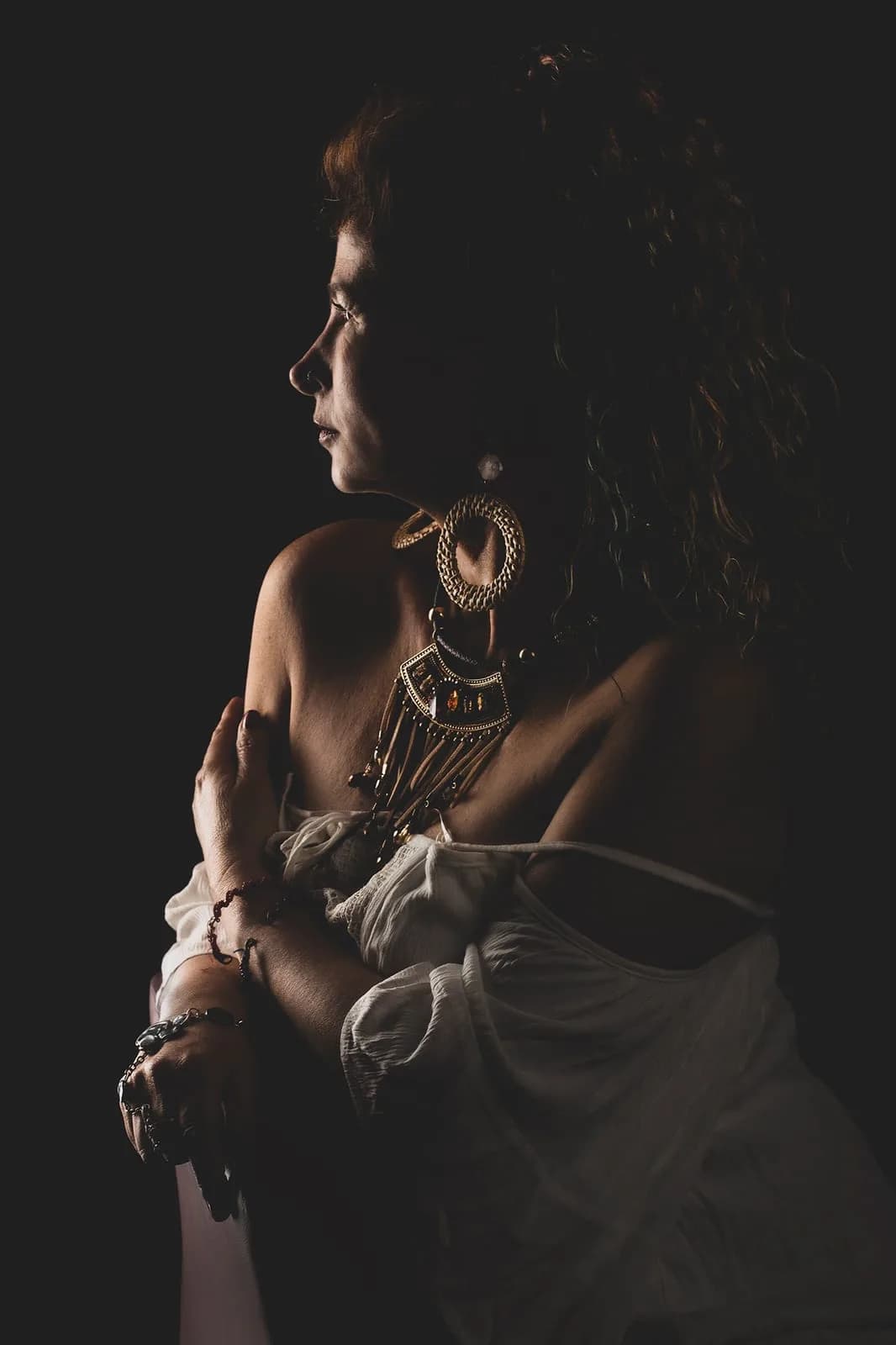 Personal portrait in profile with jewelry, side light and deep shadow — fine-art studio photography | Photo: Sharon Gabay