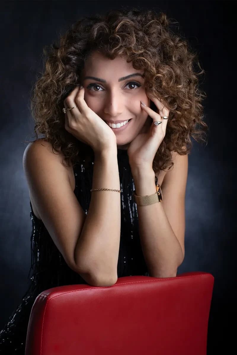 צילום סטודיו של אישה מחייכת על כיסא אדום — הזמנת צילום אצל שרון גבאי