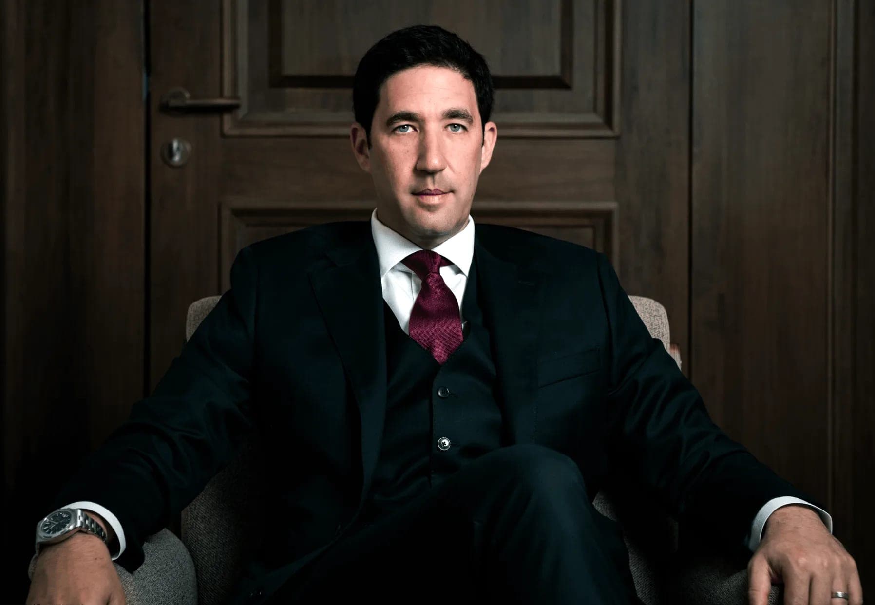The final result: a dramatic image portrait of a client in a dark suit and maroon tie, seated against a wooden door — mobile studio photography by Sharon Gabay