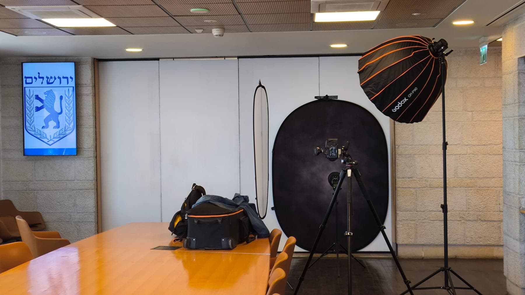 A mobile studio set up in a meeting room at Jerusalem city hall — a dark backdrop, studio lighting and a camera on a tripod, beside the Jerusalem city emblem