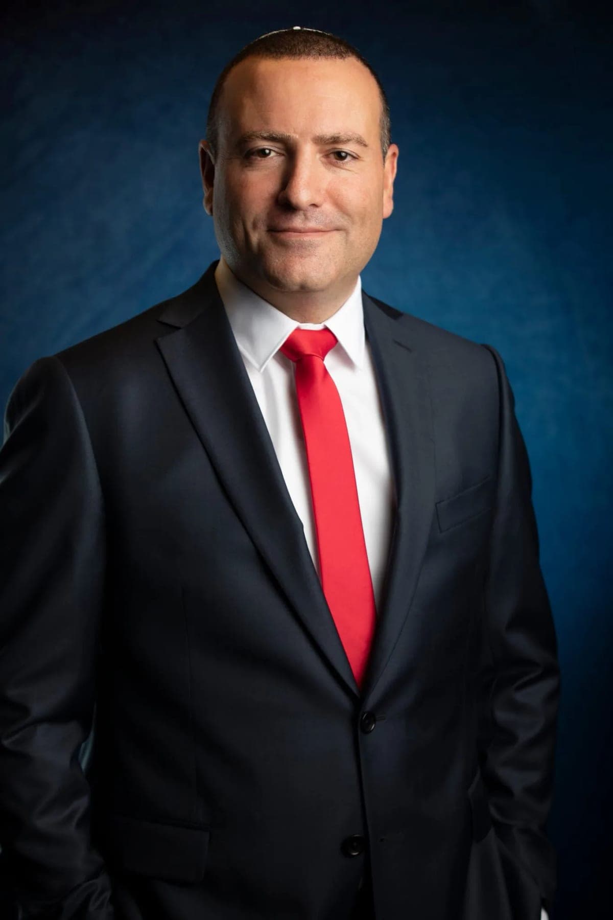 An image portrait of a public figure in a dark suit and red tie on a blue backdrop — mobile studio photography at Rehovot city hall by Sharon Gabay