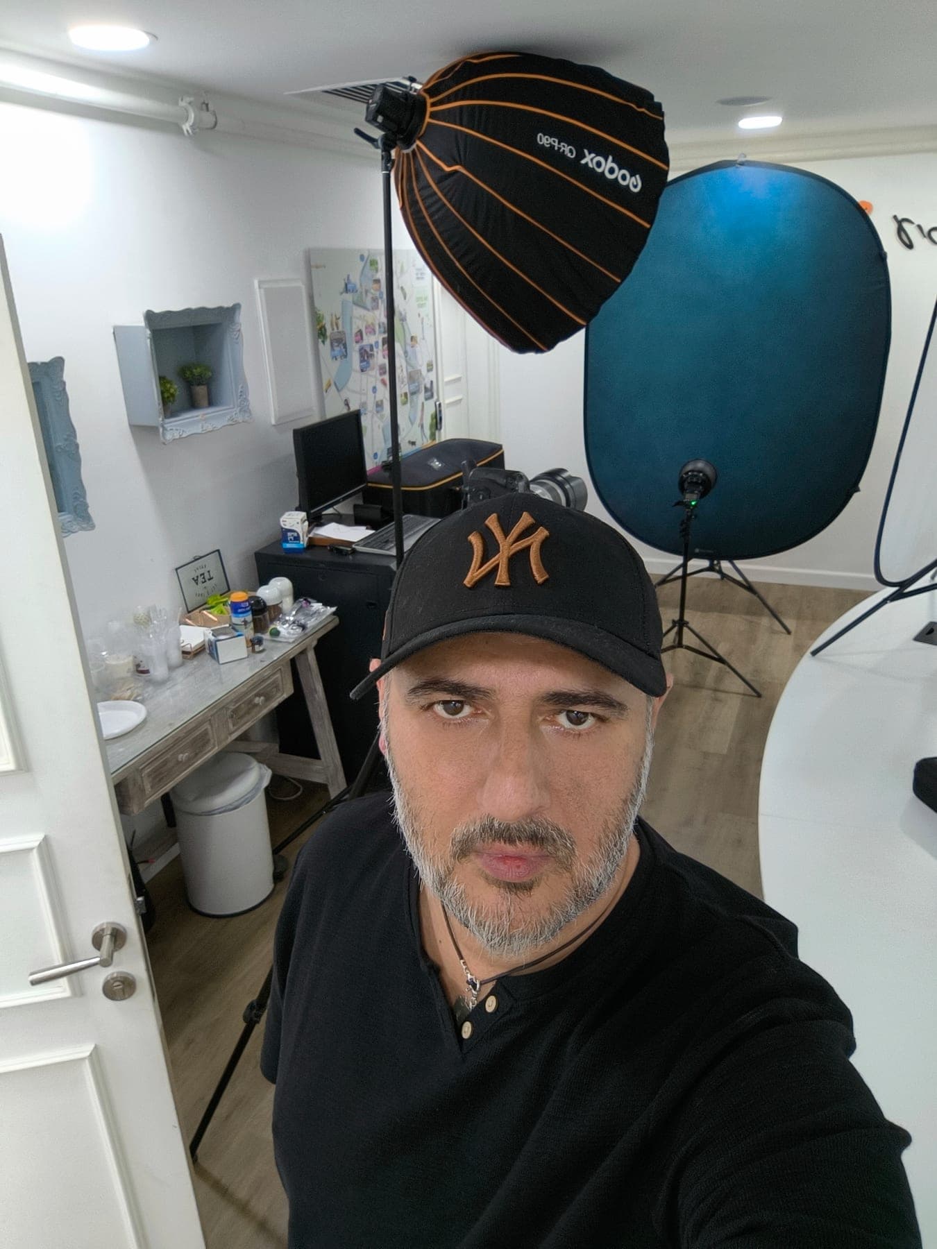 Sharon Gabay in a selfie in front of a mobile studio setup with a blue backdrop and studio lighting at the office