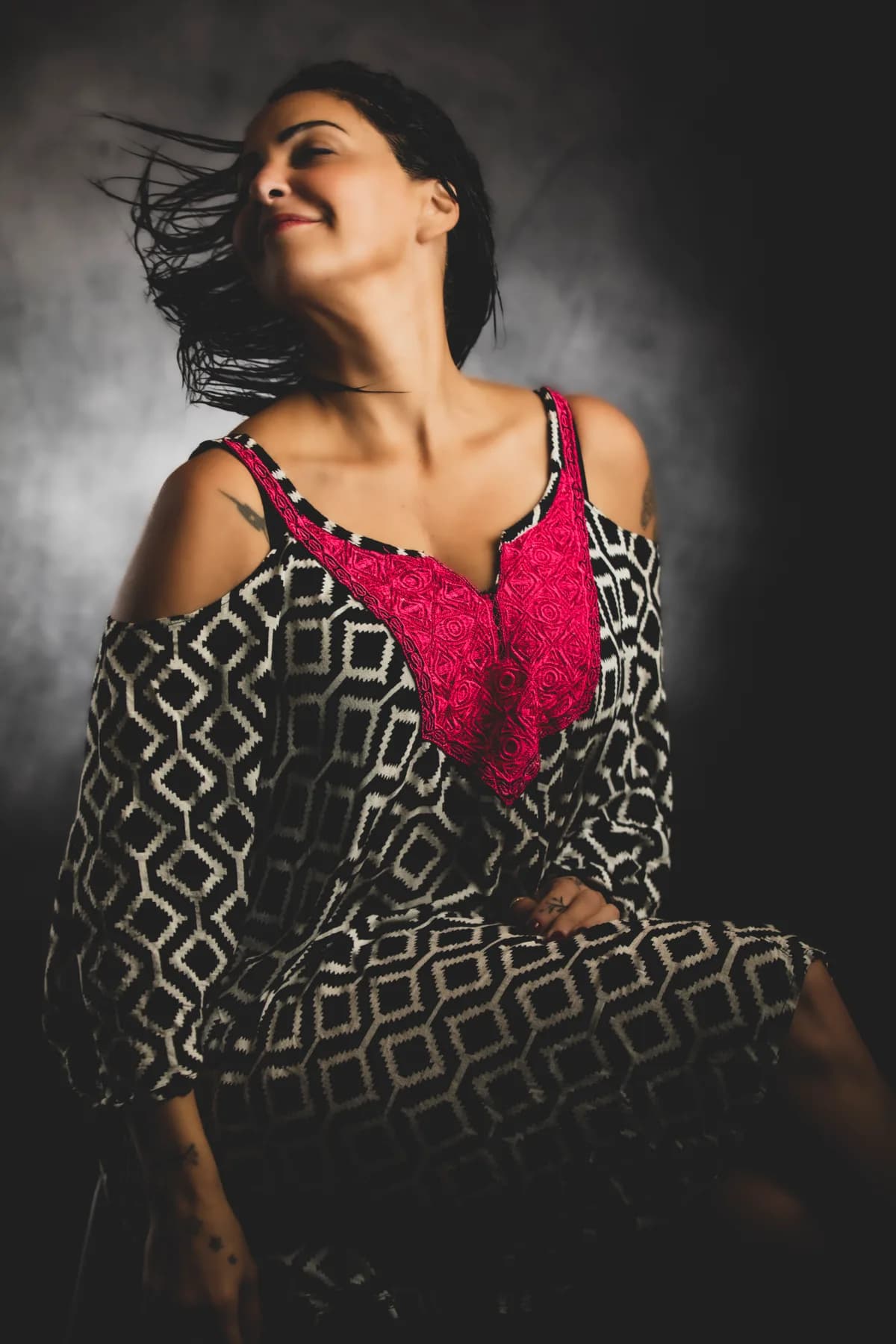Fine-art portrait of a woman in a printed dress, hair caught in the air, soft light | Photo: Sharon Gabay