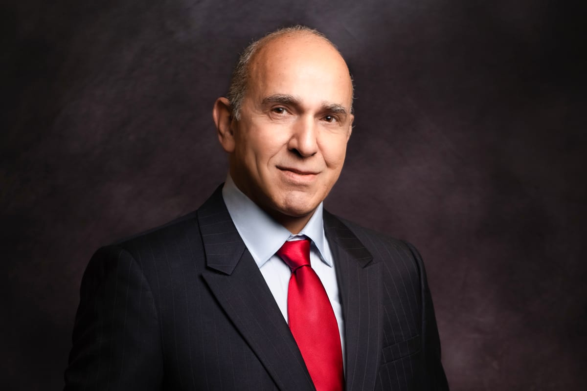 Professional headshot lit with selective light — a man in a dark suit and red tie against a dark background — Sharon Gabay