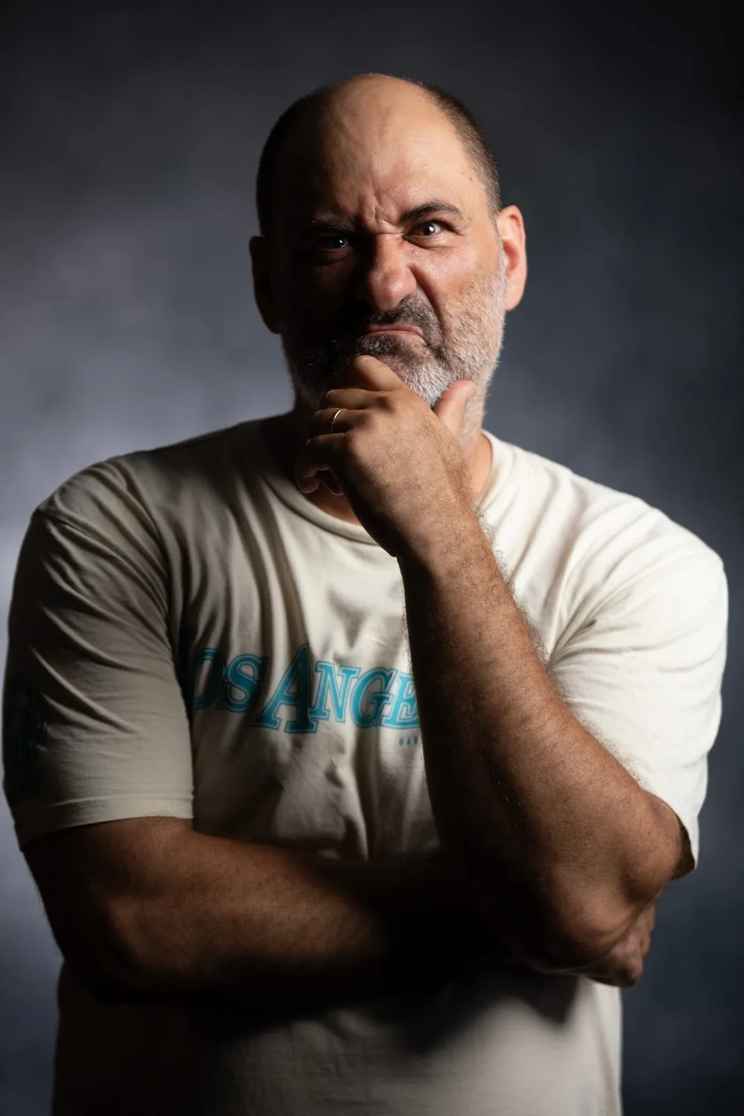 Character headshot of an actor, a man with a sly look and a hand on his chin in dramatic lighting — Sharon Gabay, headshot photographer