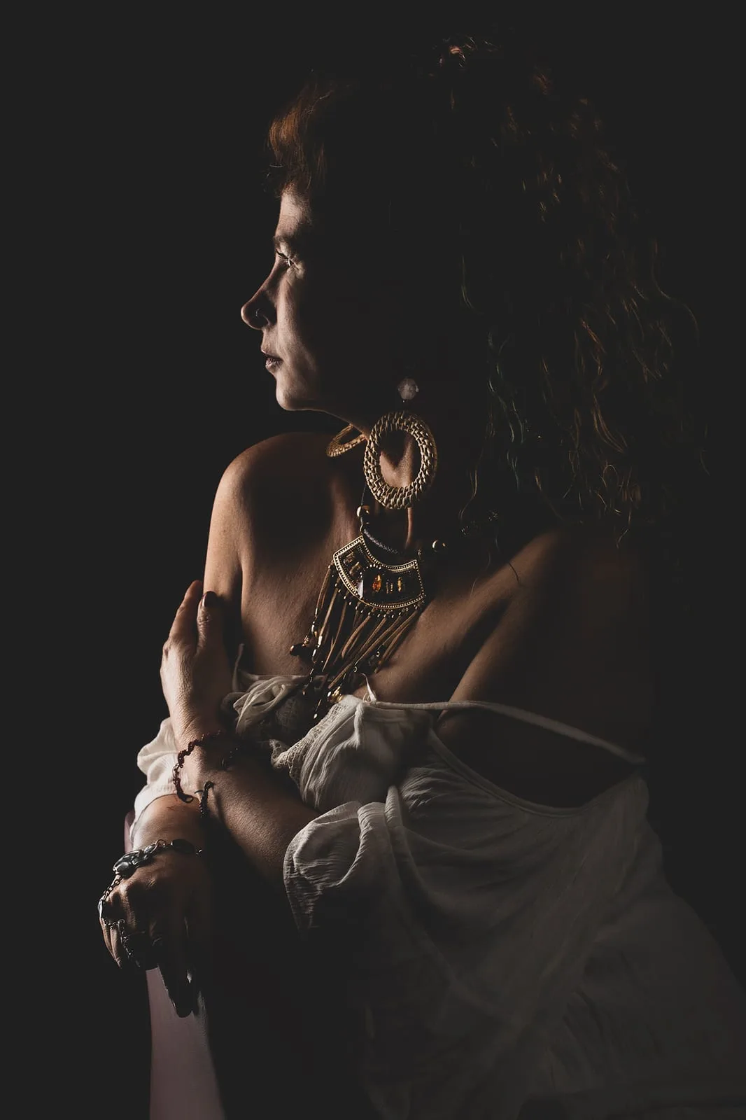 Personal portrait in profile with jewelry, side light and deep shadow — fine-art studio photography | Photo: Sharon Gabay