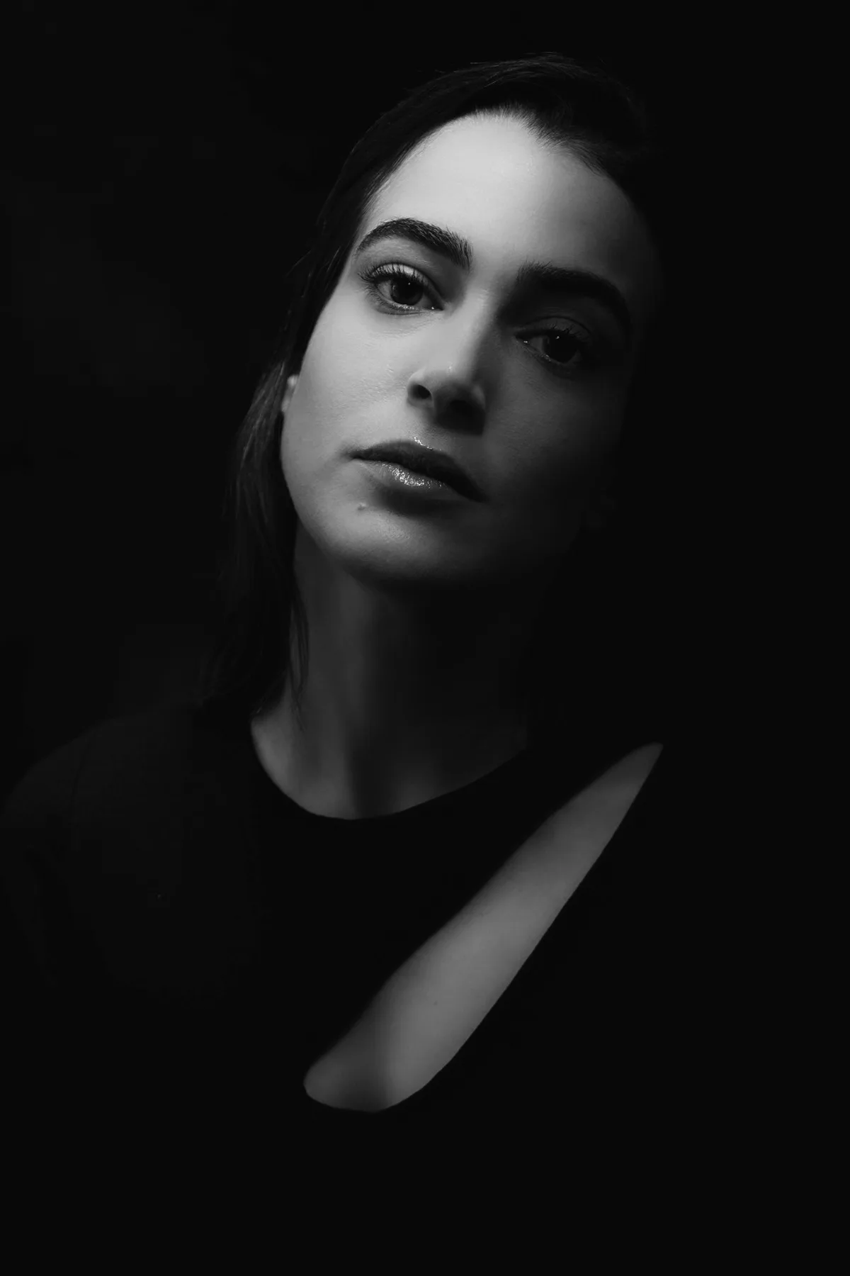 A dramatically lit studio portrait of actress Nitzan Shik, one side of her face glowing and the other dissolving into shadow — Sharon Gabay, portrait photographer