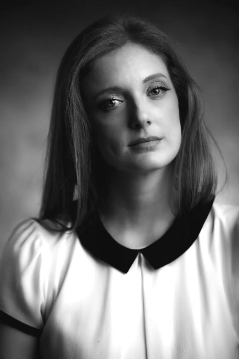 Black-and-white personal portrait of a young woman in a white-collared dress, a calm gaze into the camera | Photo: Sharon Gabay