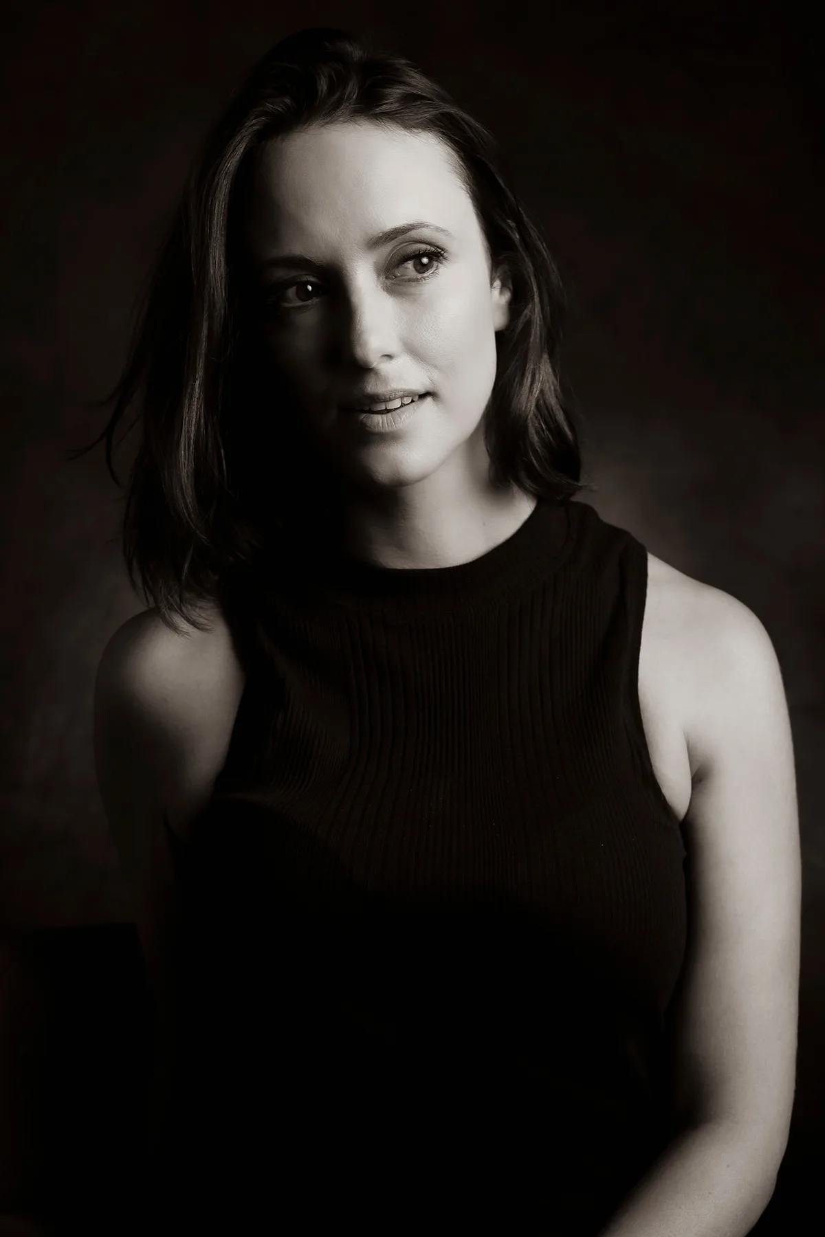 Black-and-white personal portrait of a woman in a dark top, bare shoulders and clean light | Photo: Sharon Gabay