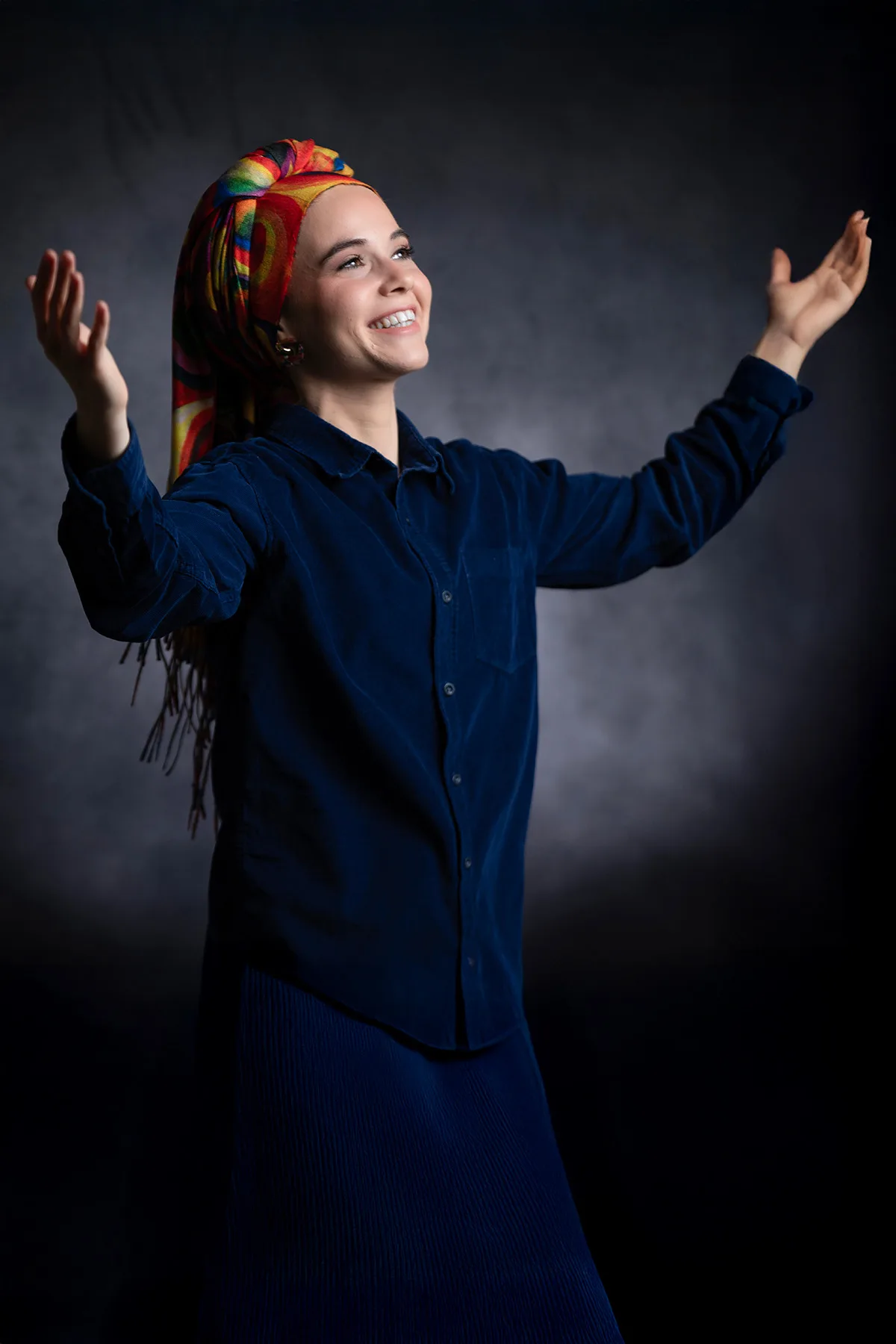 Headshot of a woman in a colorful headscarf, arms open, in motion | Photo: Sharon Gabay