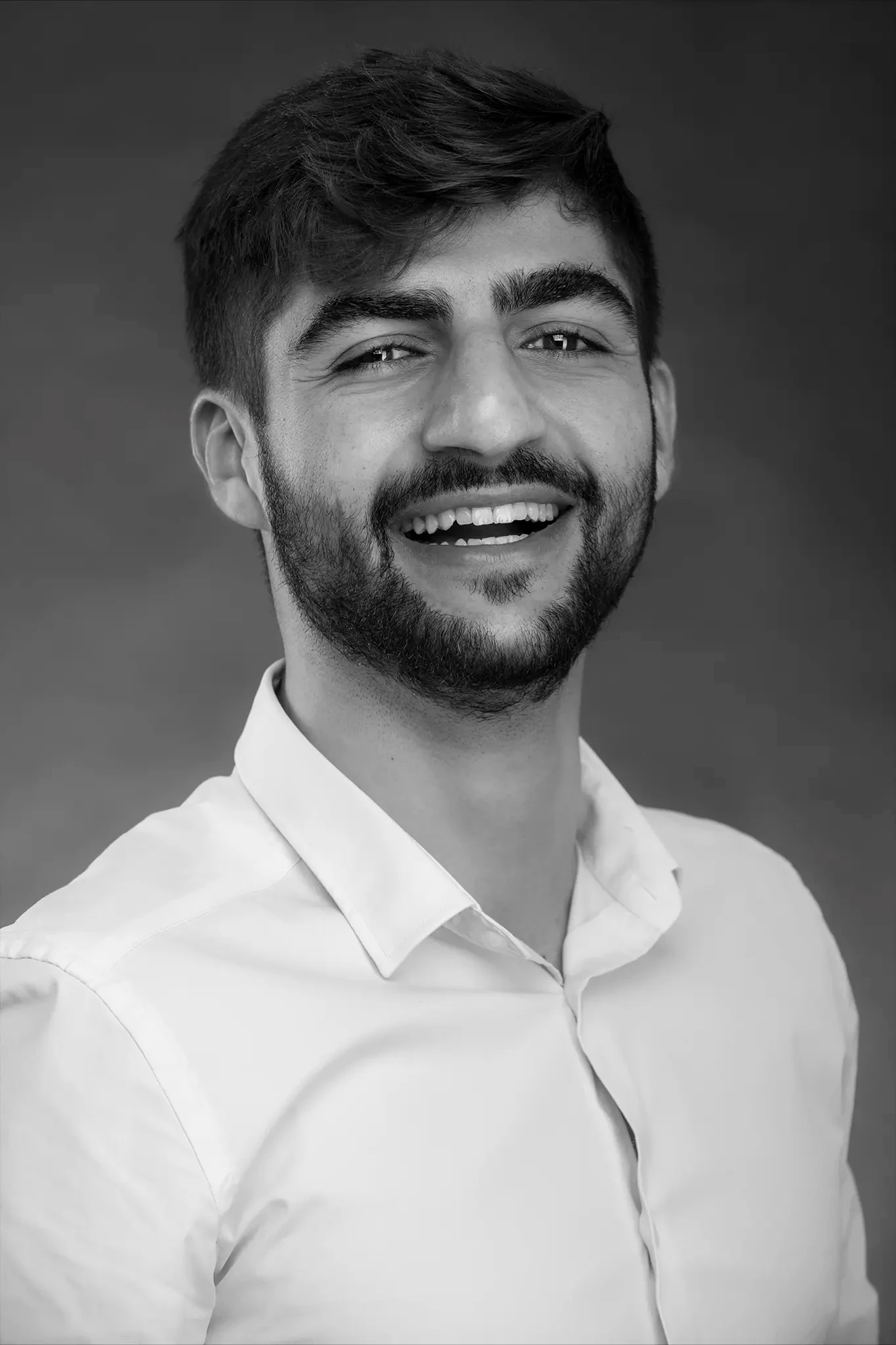 Black-and-white headshot of a young man in a genuine laugh — documentary expression in Sharon Gabay's studio