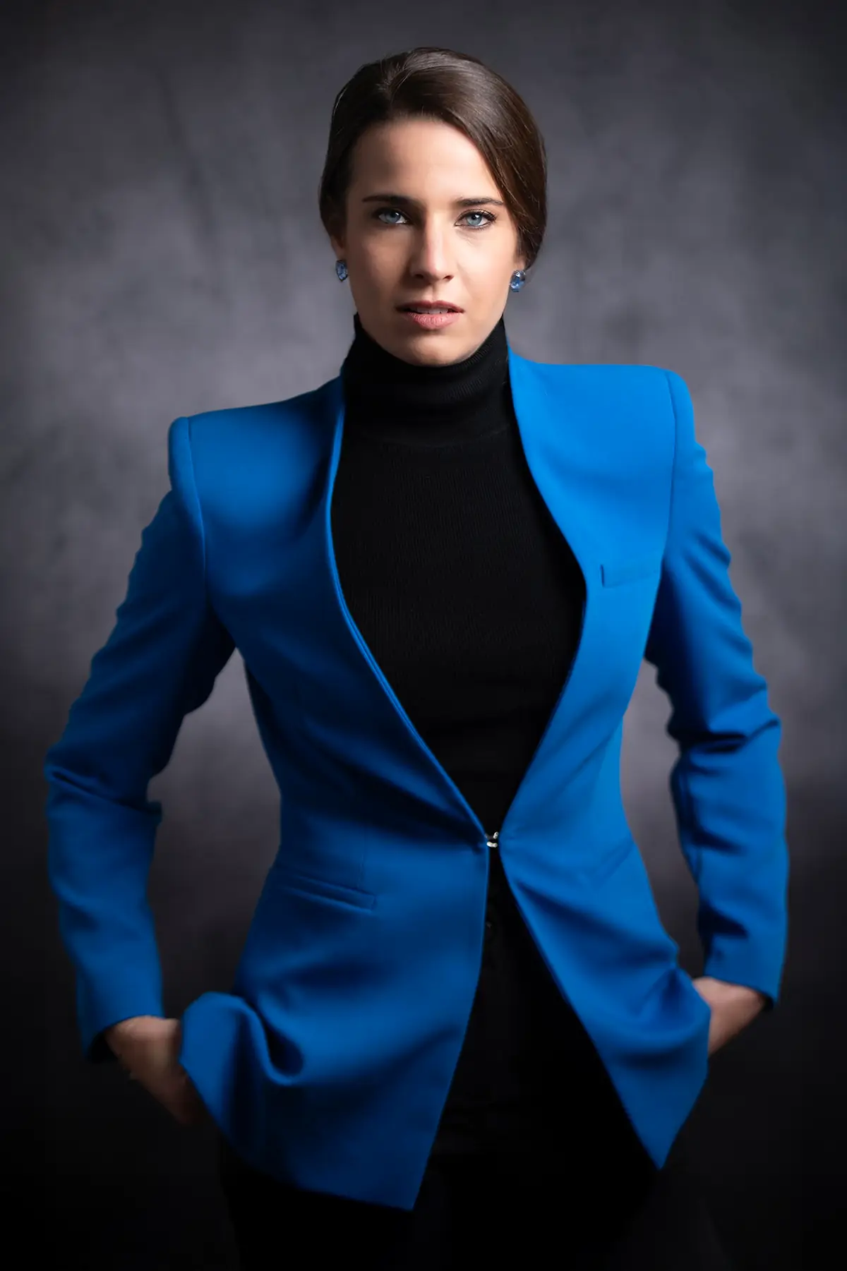 Headshot of a professional woman in a blue blazer and black turtleneck, direct gaze on a dark backdrop | Photo: Sharon Gabay
