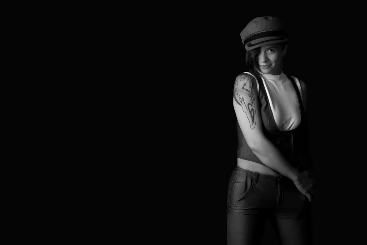Black-and-white personal portrait of a woman in a flat cap, a lone figure in the black | Photo: Sharon Gabay