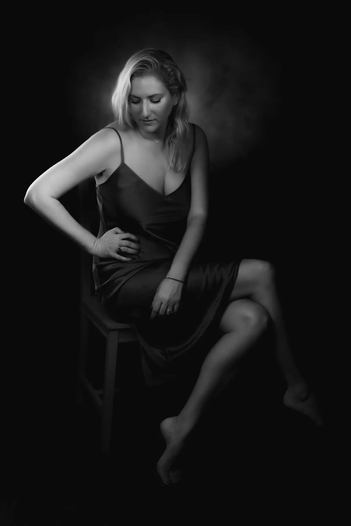 Black-and-white personal portrait of a seated woman in the studio, side light and deep shadow | Photo: Sharon Gabay