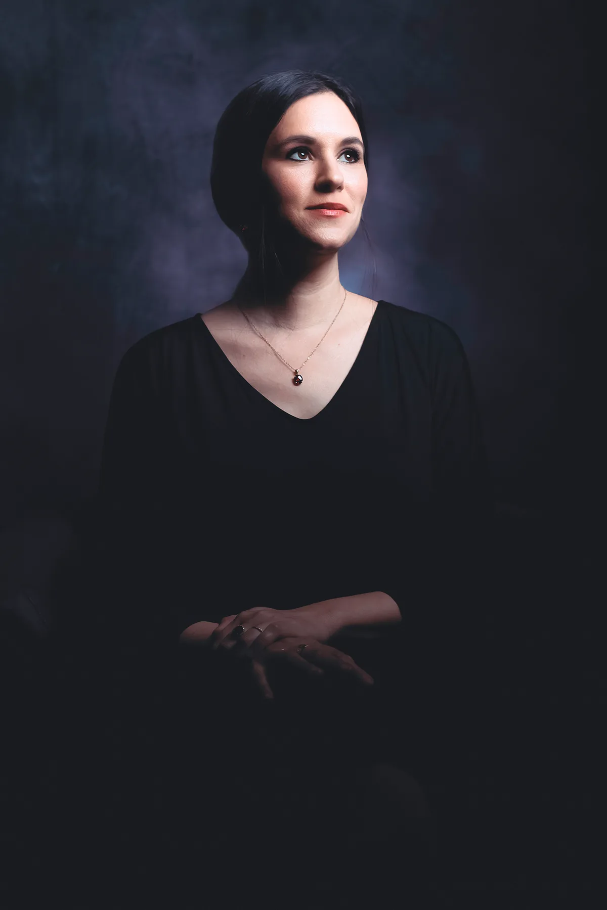 A quiet personal portrait in black against a dark backdrop — soft light on the face and hands | Photo: Sharon Gabay