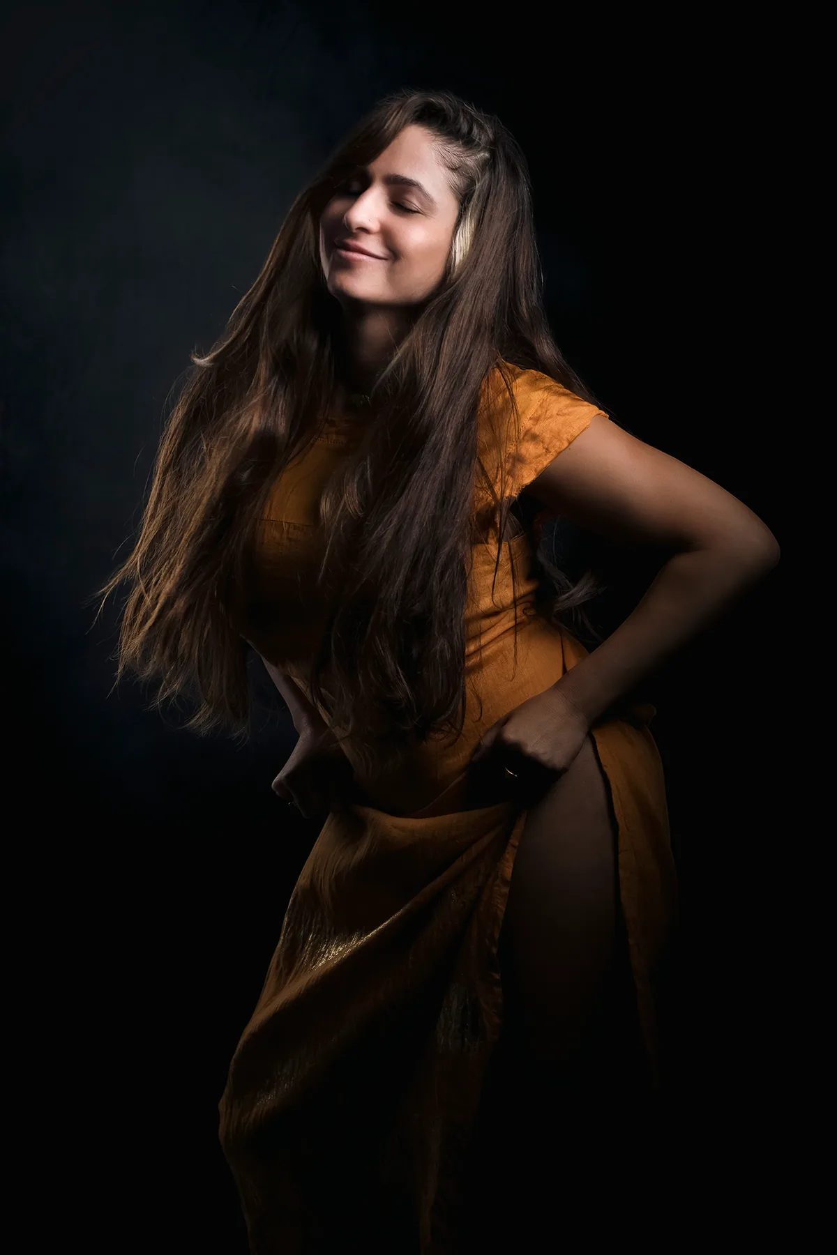Personal portrait of a woman in a golden dress, long hair and warm light against a dark backdrop | Photo: Sharon Gabay