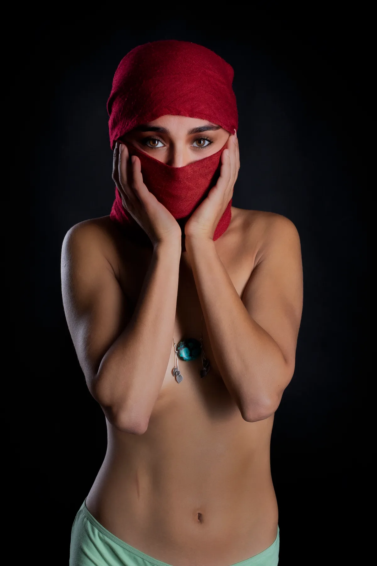 Fine-art portrait of a woman in a red scarf against a black background, soft light on her face | Photo: Sharon Gabay