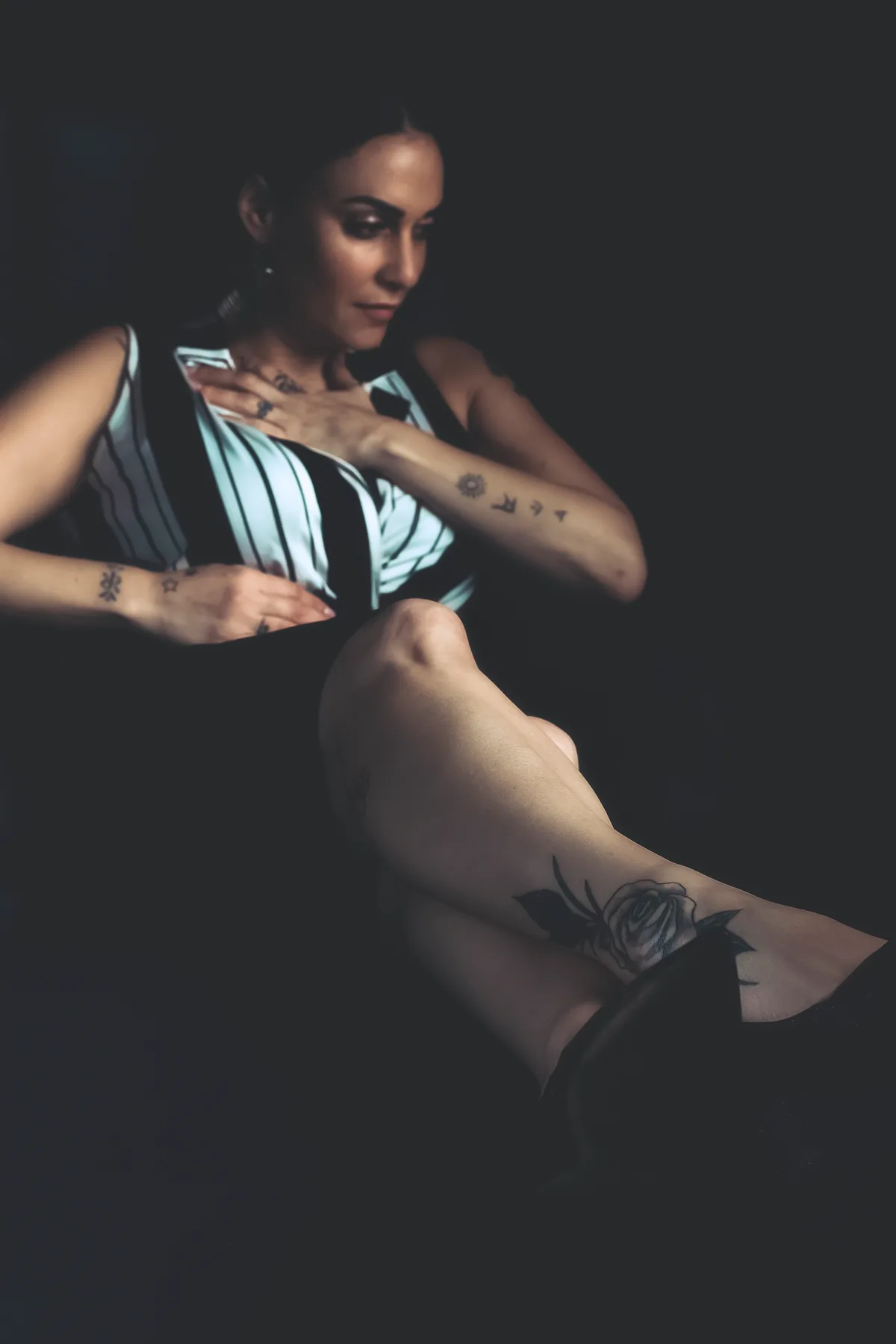 Personal portrait of a woman in a striped shirt in a relaxed pose, low light and a dark backdrop | Photo: Sharon Gabay