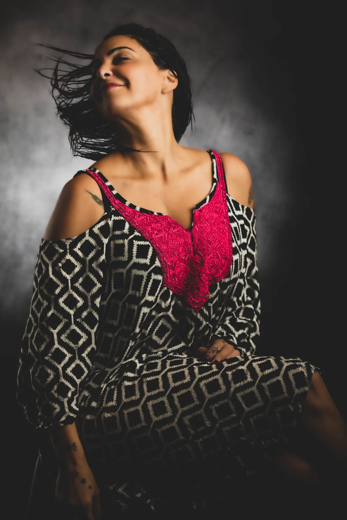 Fine-art portrait of a woman in a printed dress, hair caught in the air, soft light | Photo: Sharon Gabay