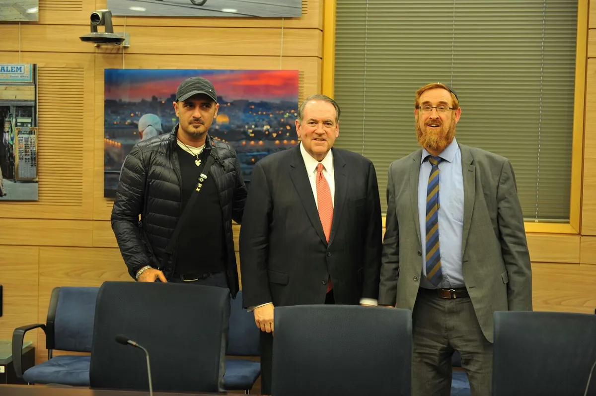 Sharon Gabay, Mike Huckabee and MK Yehudah Glick at the Knesset exhibition, a Jerusalem panorama behind them, 2017